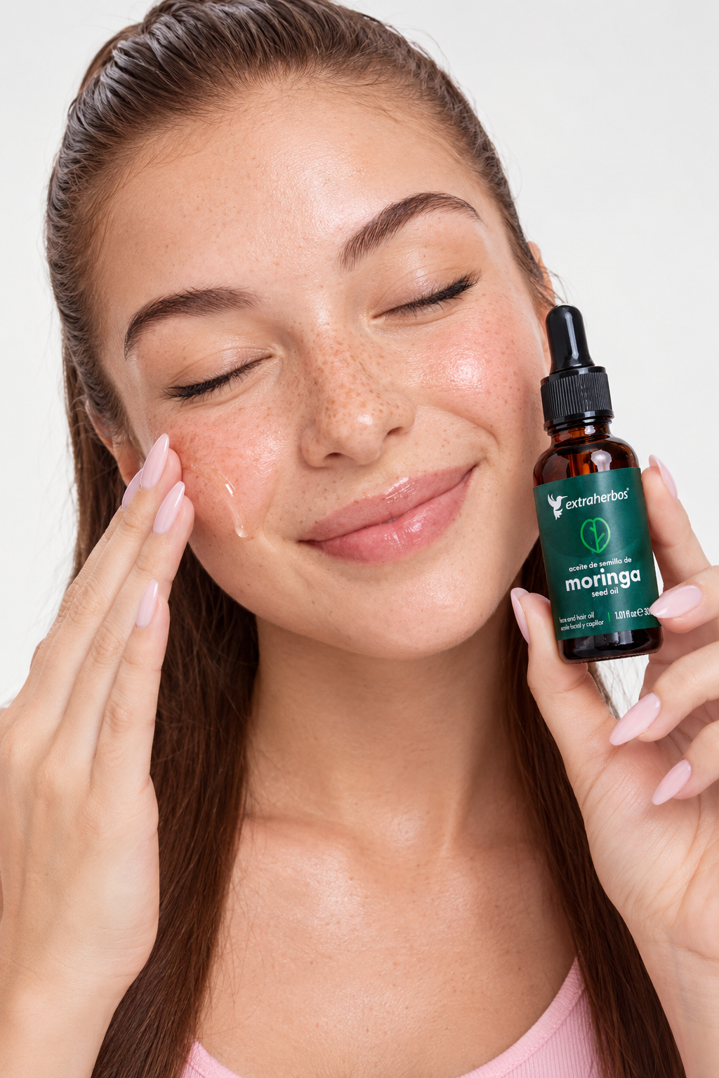 Mujer aplicando aceite de Moringa Extraherbos y sosteniendo el frasco